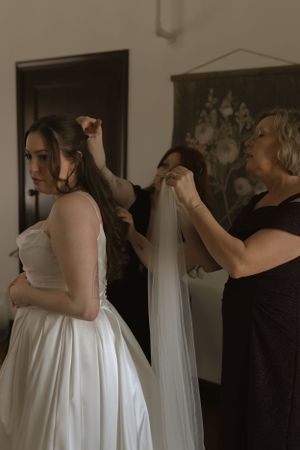 A bride in a white wedding gown gets her veil adjusted during preparation.