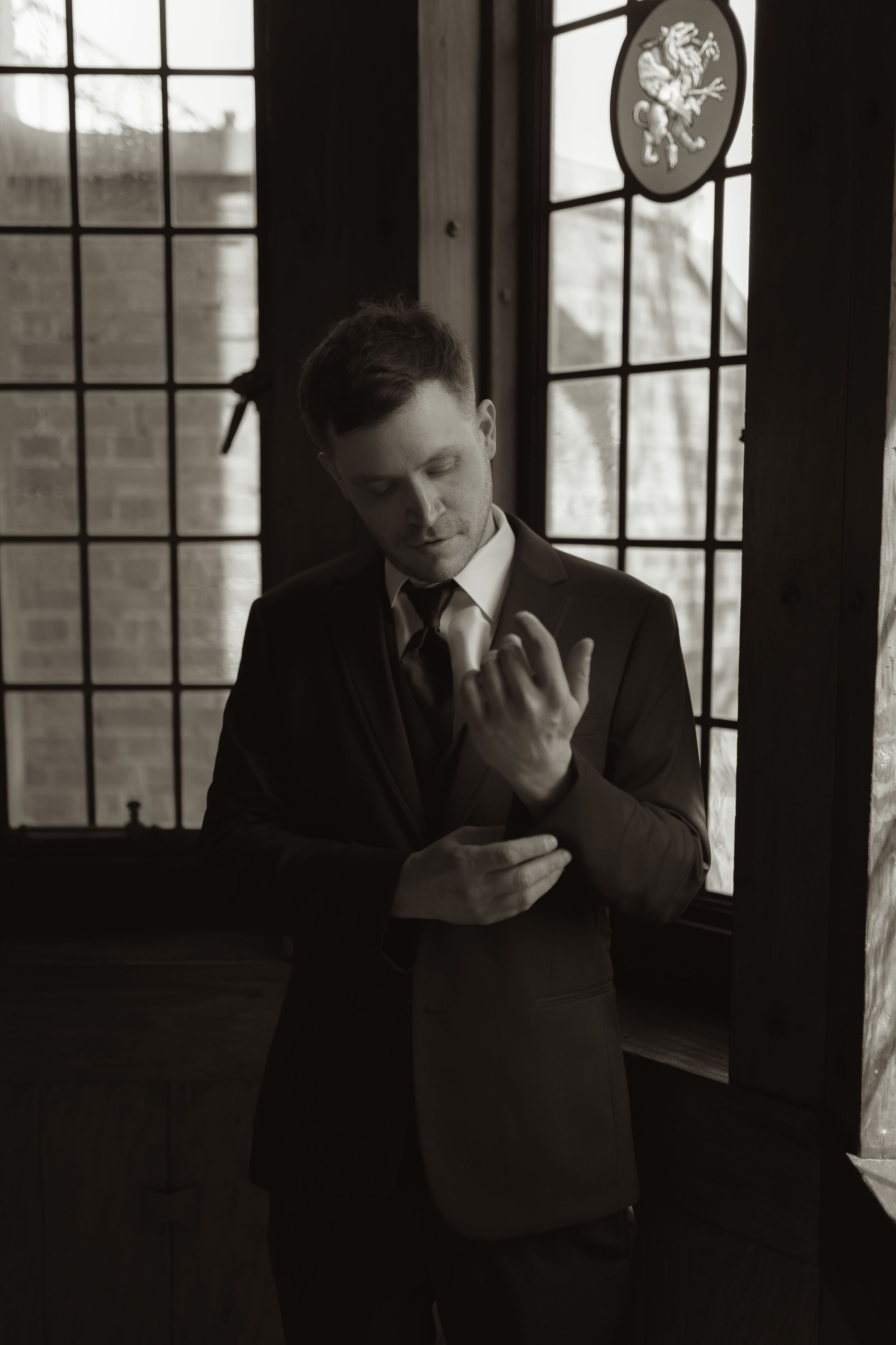 Man in formal attire shows emotional distress in a dark room with window light.