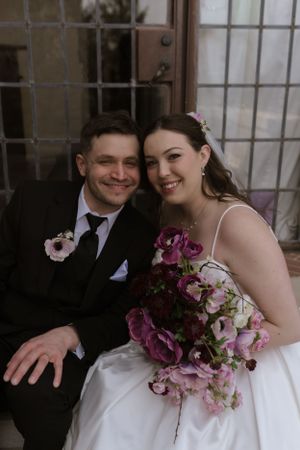 A joyful wedding portrait featuring purple flowers and a classic white gown.