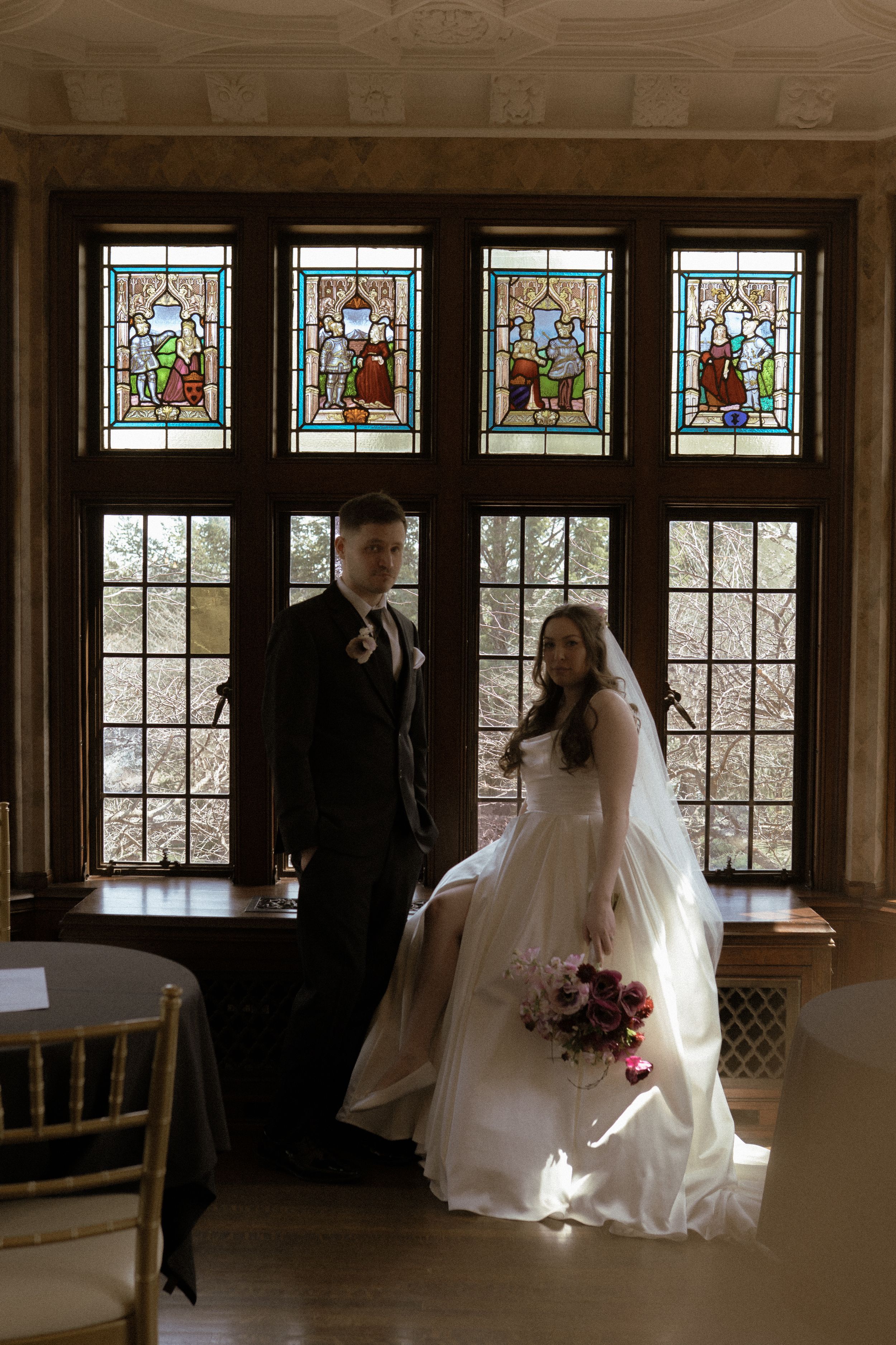 Wedding couple poses in front of stained glass windows in elegant indoor setting.