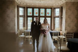 A wedding ceremony setup in an elegant room with bay windows and chiavari chairs.