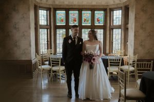 A romantic wedding ceremony takes place in an elegant room with large windows and natural light.