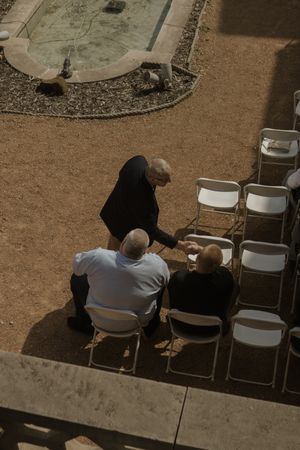 Wedding guests seated in white folding chairs on a rustic outdoor patio.