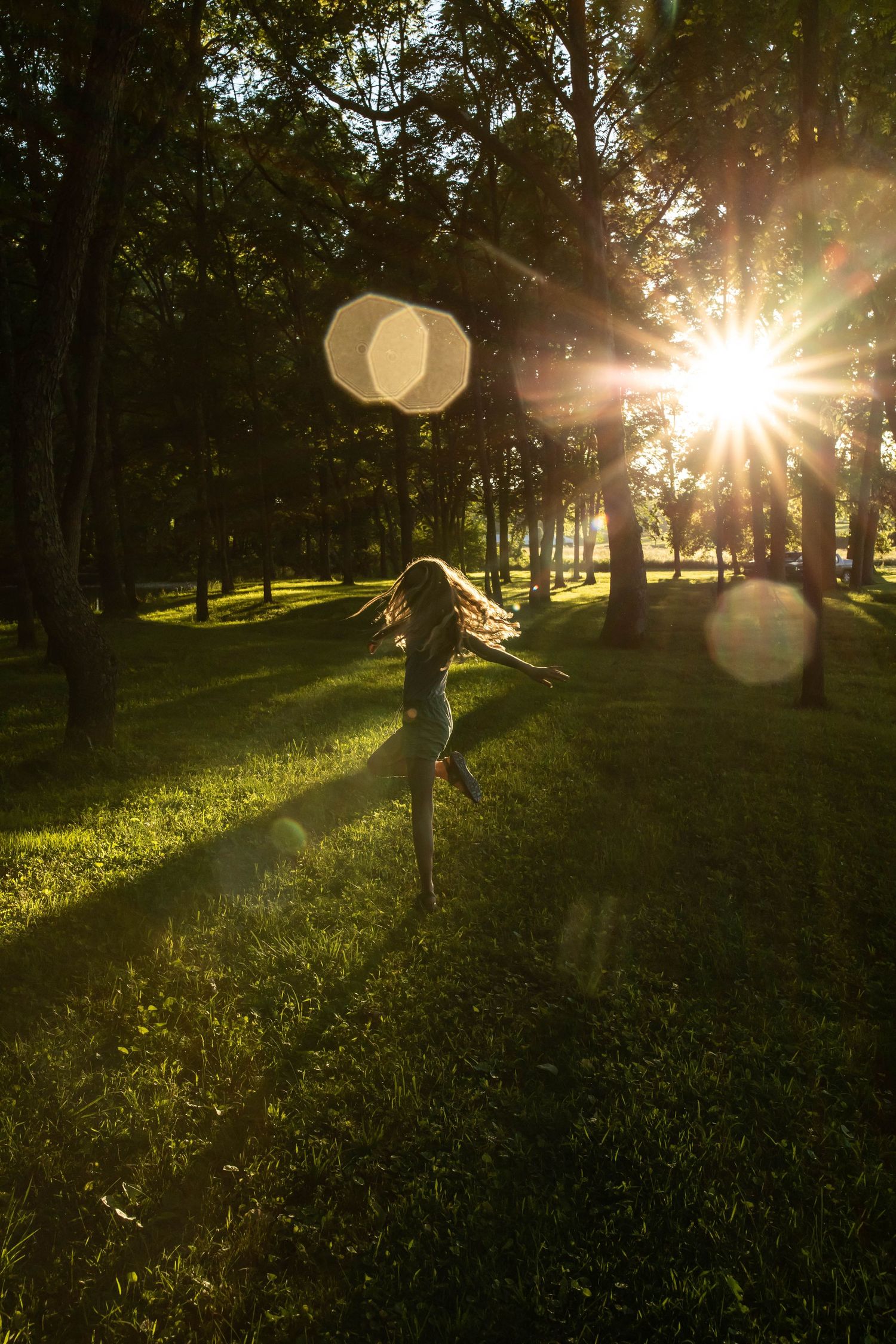 Photo of a girl dancing in the forest at sunset while sun flare comes through the trees