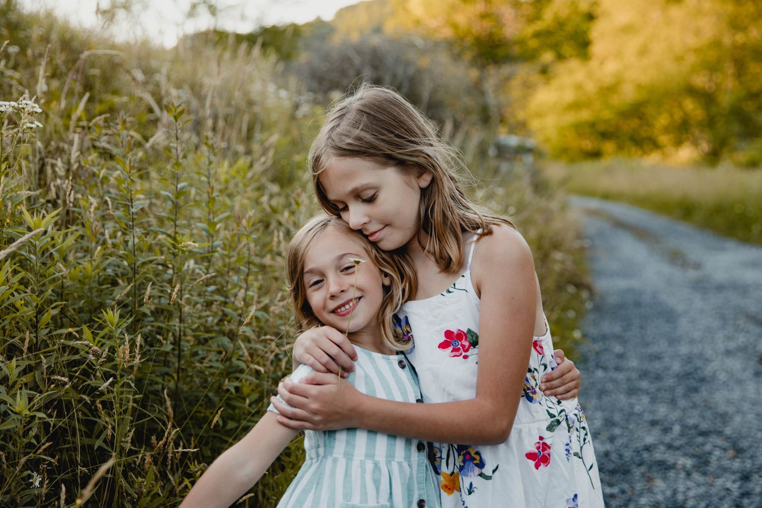 Image of two sisters hugging while standing in a field of flowers along a dirt road during family photos on a mountain in Fall