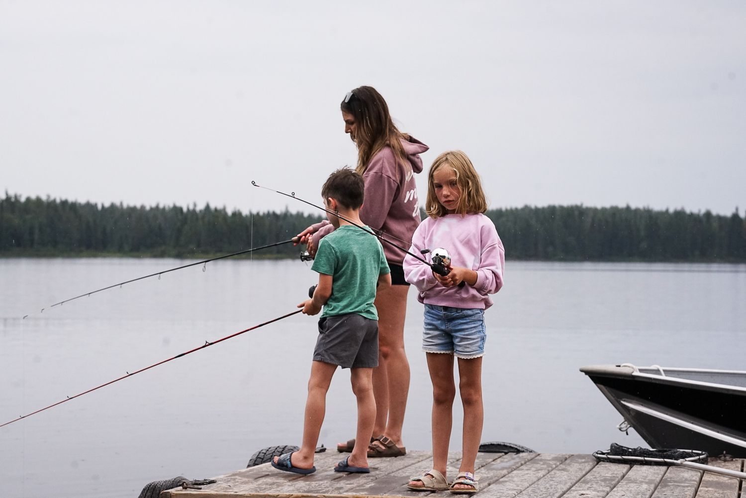 Two people fish from a wooden dock on a misty lake during a peaceful summer day.