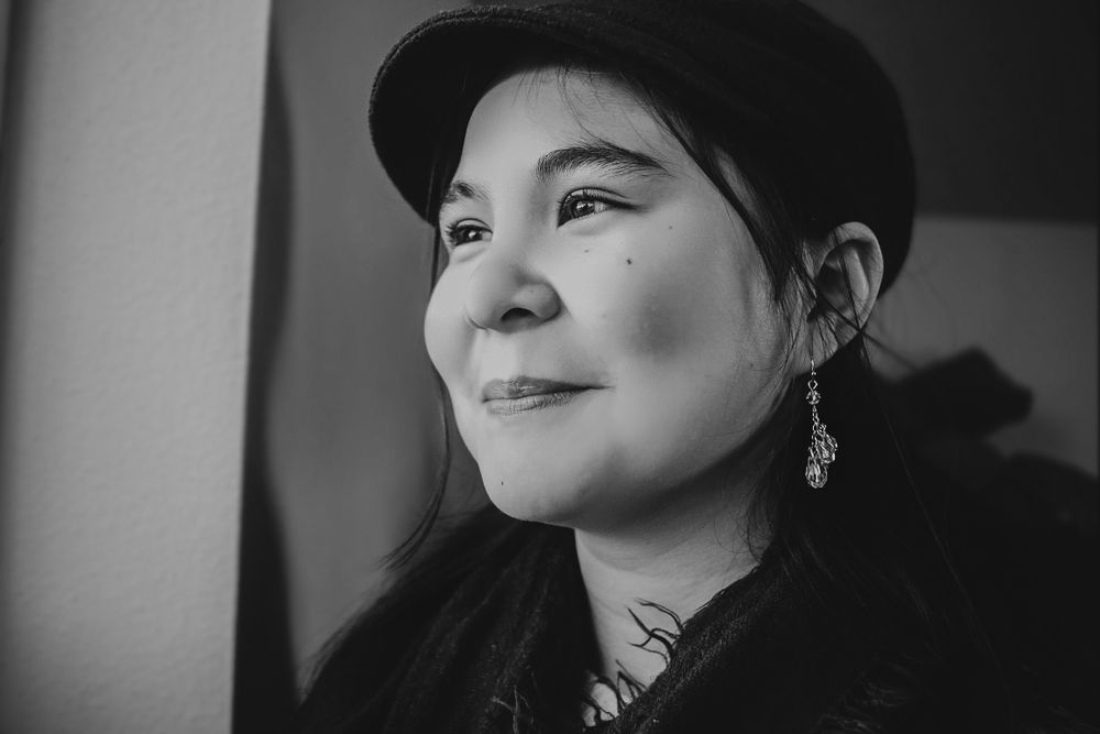 Black and white close-up portrait of woman in black cap looking upward thoughtfully.
