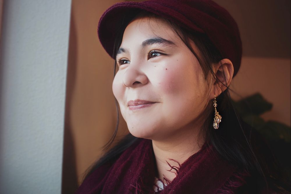 Close-up portrait of smiling woman in burgundy cap and scarf gazing upward in warm light.