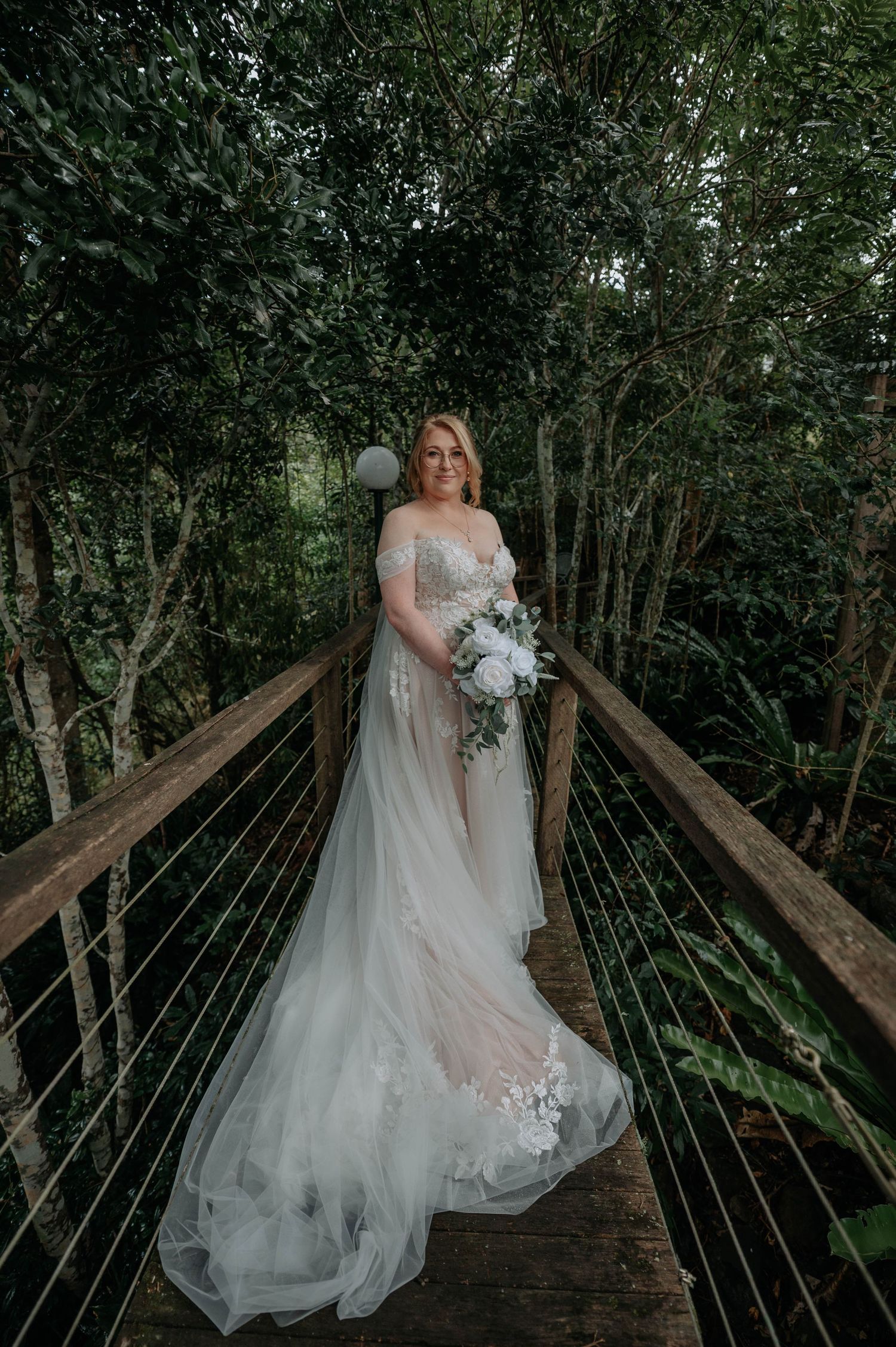 An elegant bridal portrait on a wooden walkway surrounded by dense forest foliage.