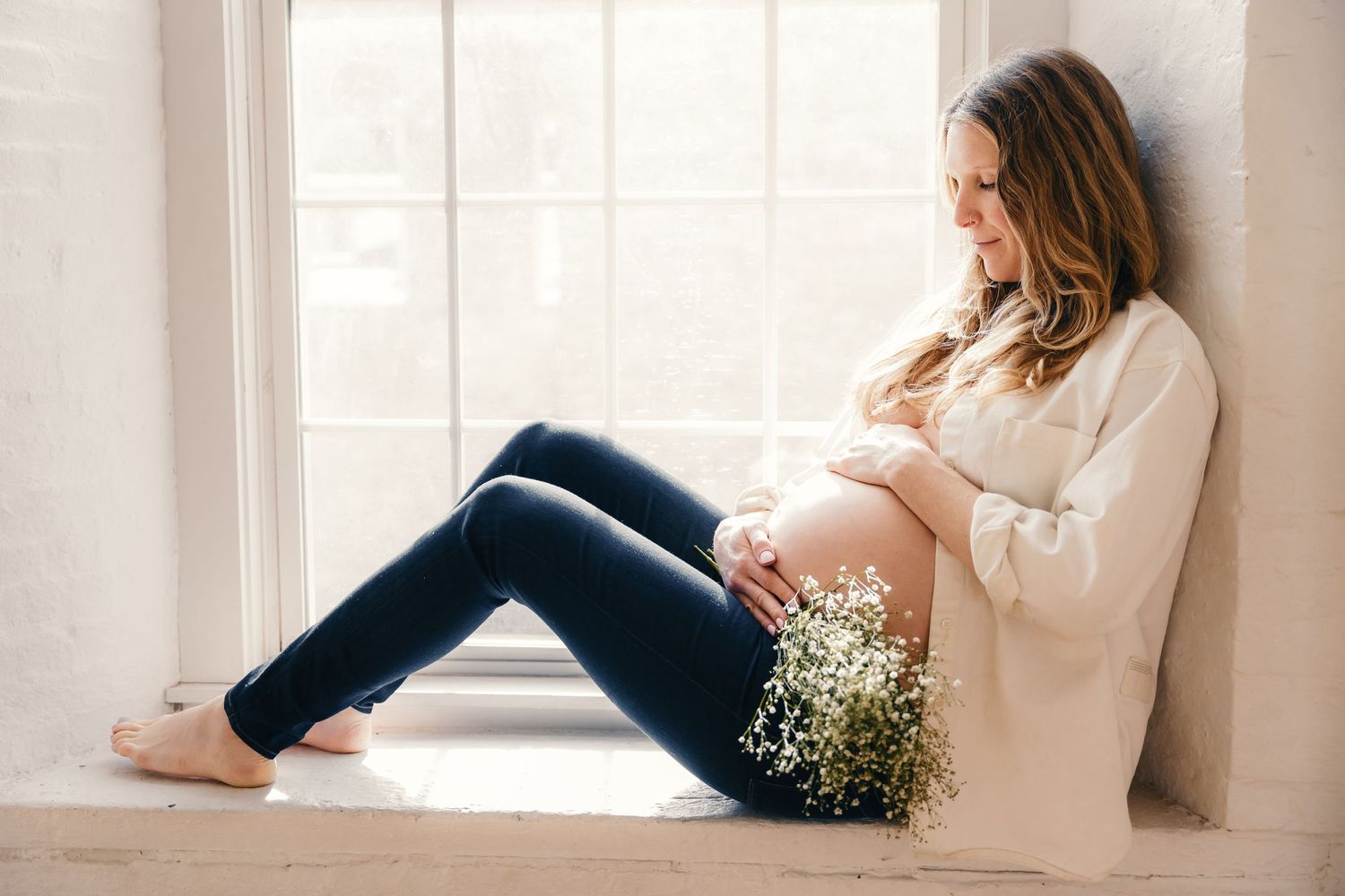 Woman in white sweater sitting by window with natural light streaming in.