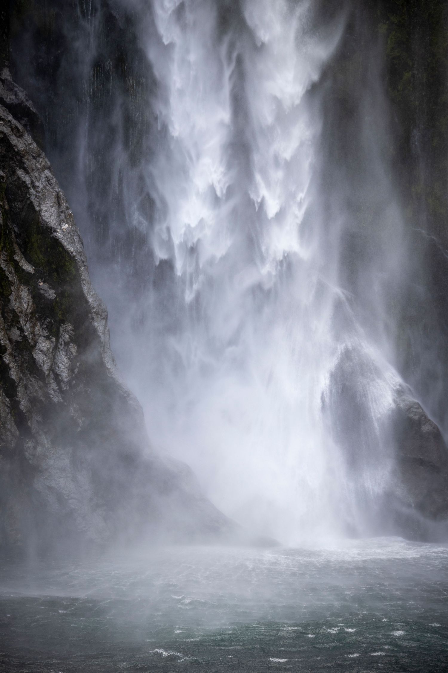 Tall waterfall cascading down rocky cliffs into a misty turquoise pool, with spray and motion captured in soft natural light.