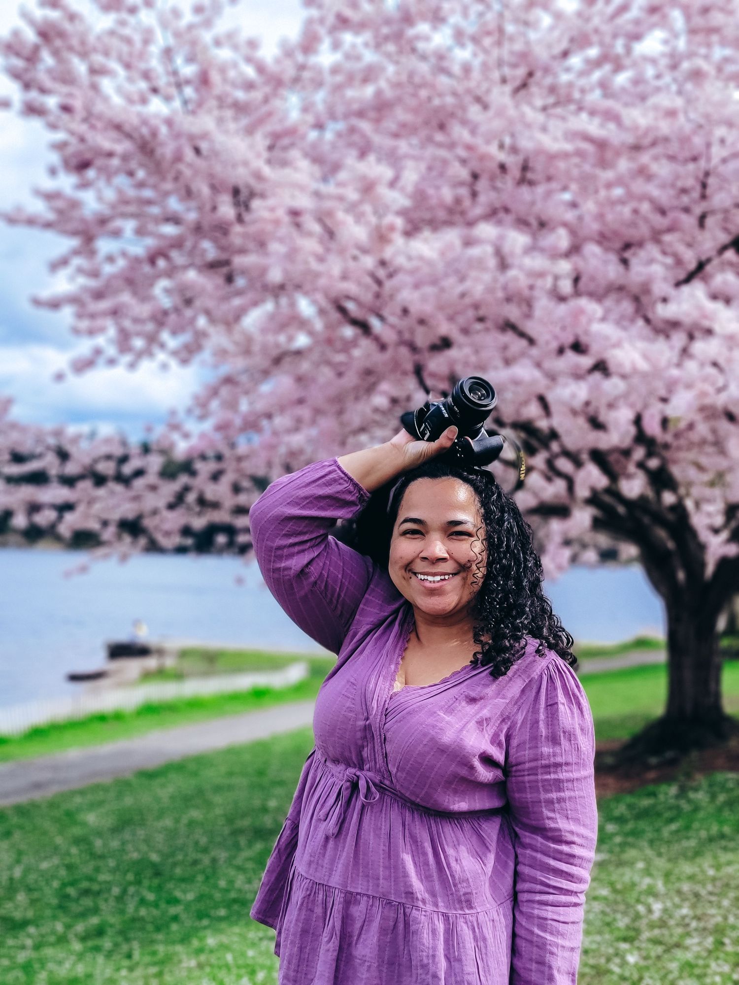 Woman in a purple dress posing under a blooming cherry blossom tree near a peaceful lake washington Seattle. Elegant spring photo session.