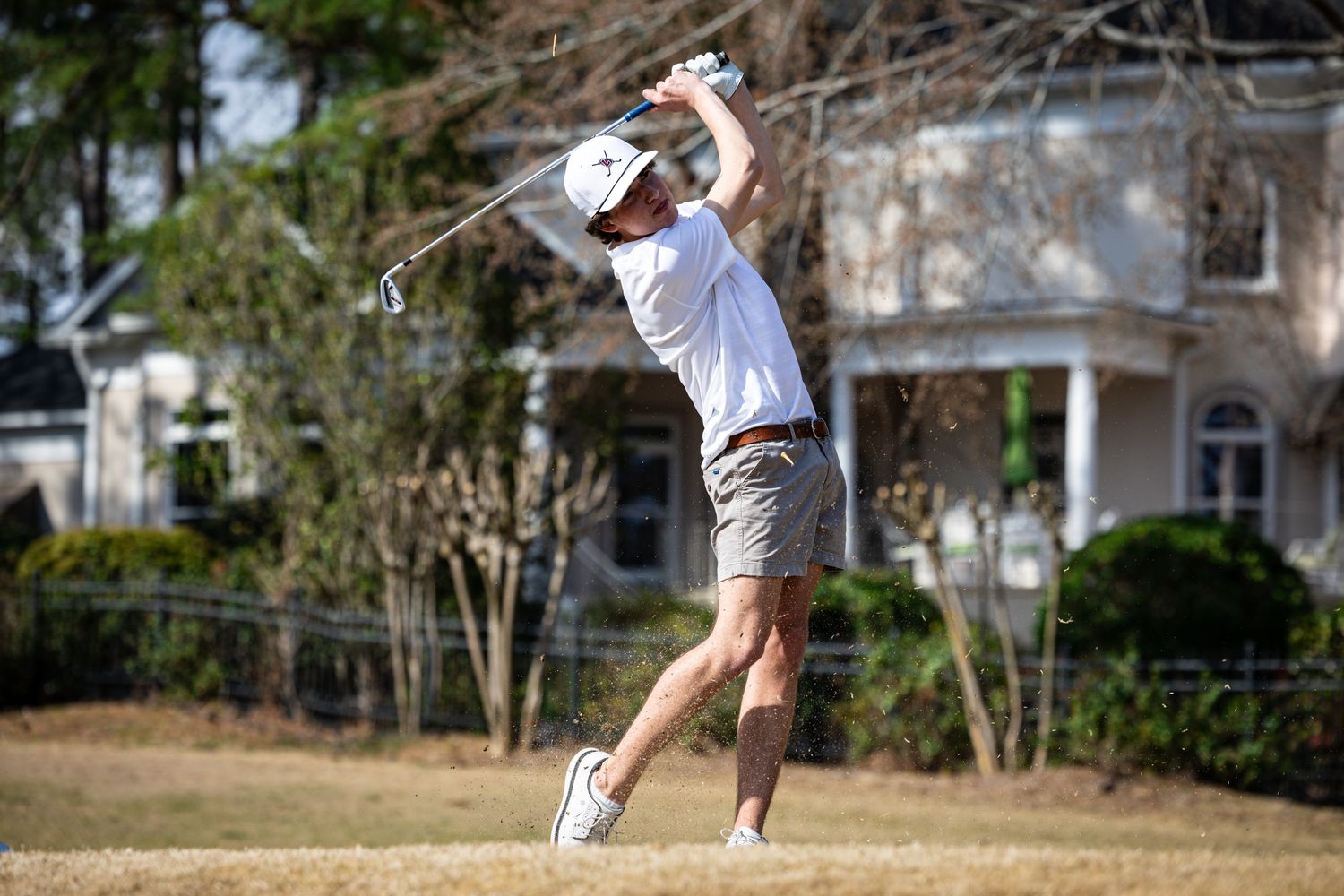 Golfer in light colored outfit follows through on swing during sunny day.