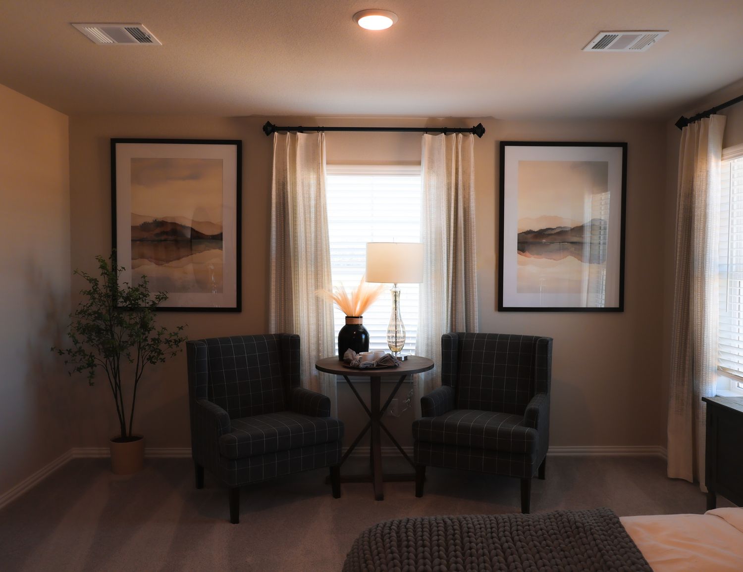 Cozy sitting area with two dark chairs, landscape artwork, and natural light from windows.