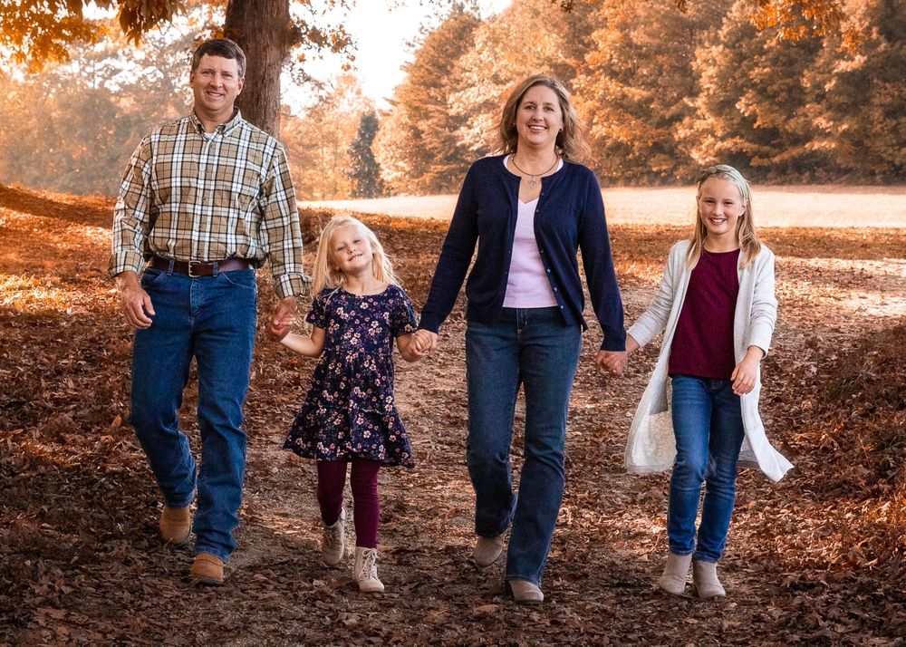 Family walking together on an autumn path covered in fallen leaves.