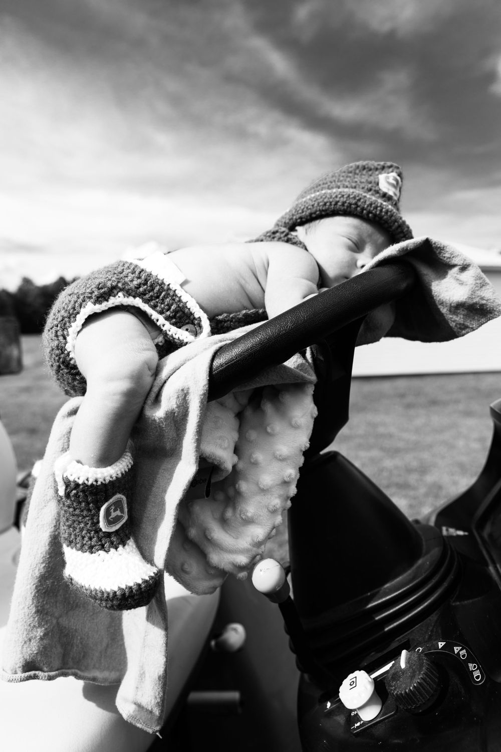 A black and white photo of a baby in knitted cowboy attire sleeping on a saddle.