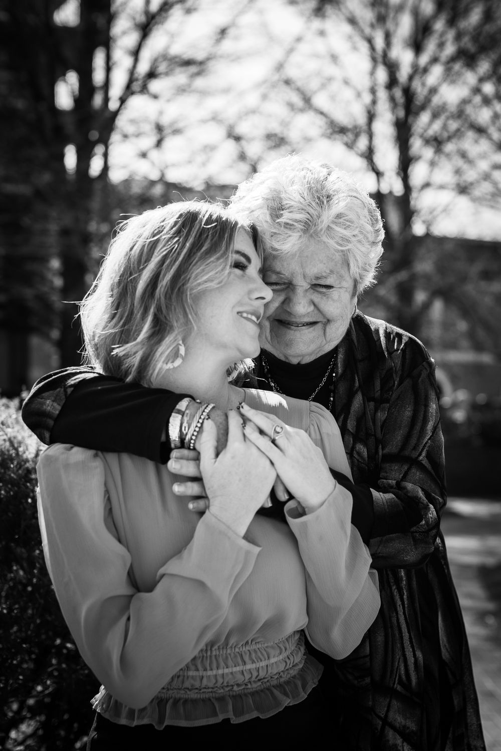 Black and white photo of elderly woman hugging younger blonde woman outdoors, sharing a warm, joyful embrace.