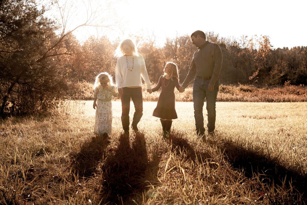 A family of four holding hands while walking into the sunset creating long shadows.