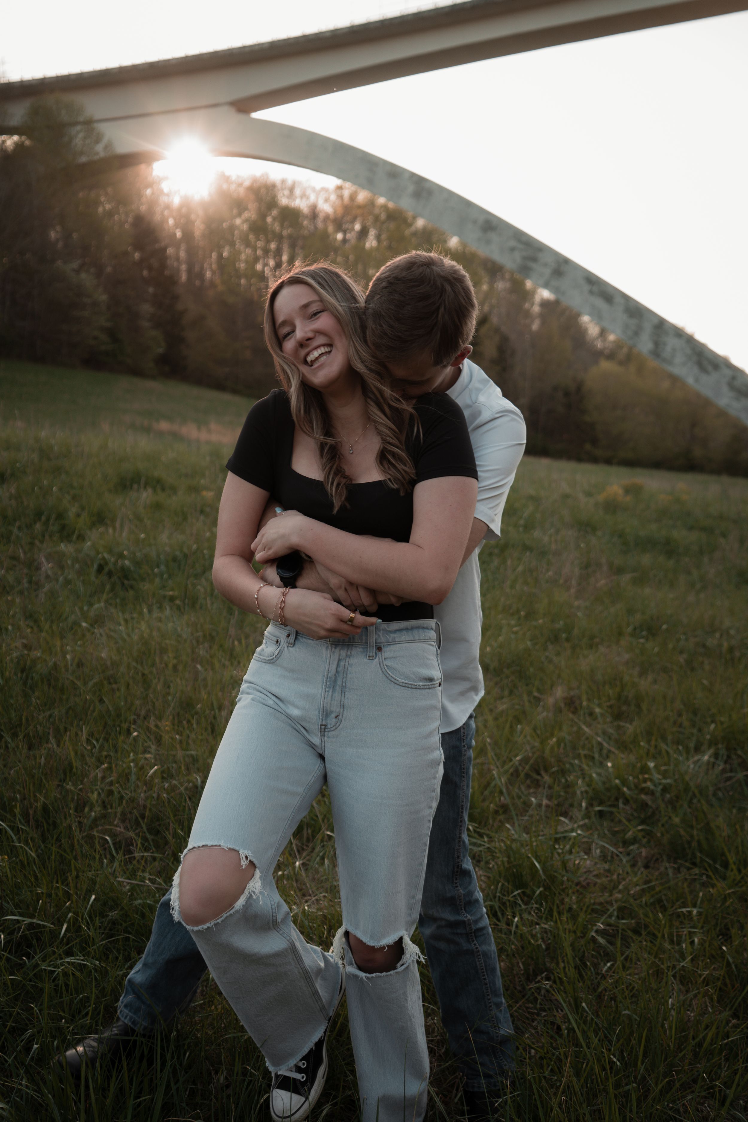 A romantic couple embraces in a sunlit meadow during golden hour, creating a series of candid moments in ripped jeans.