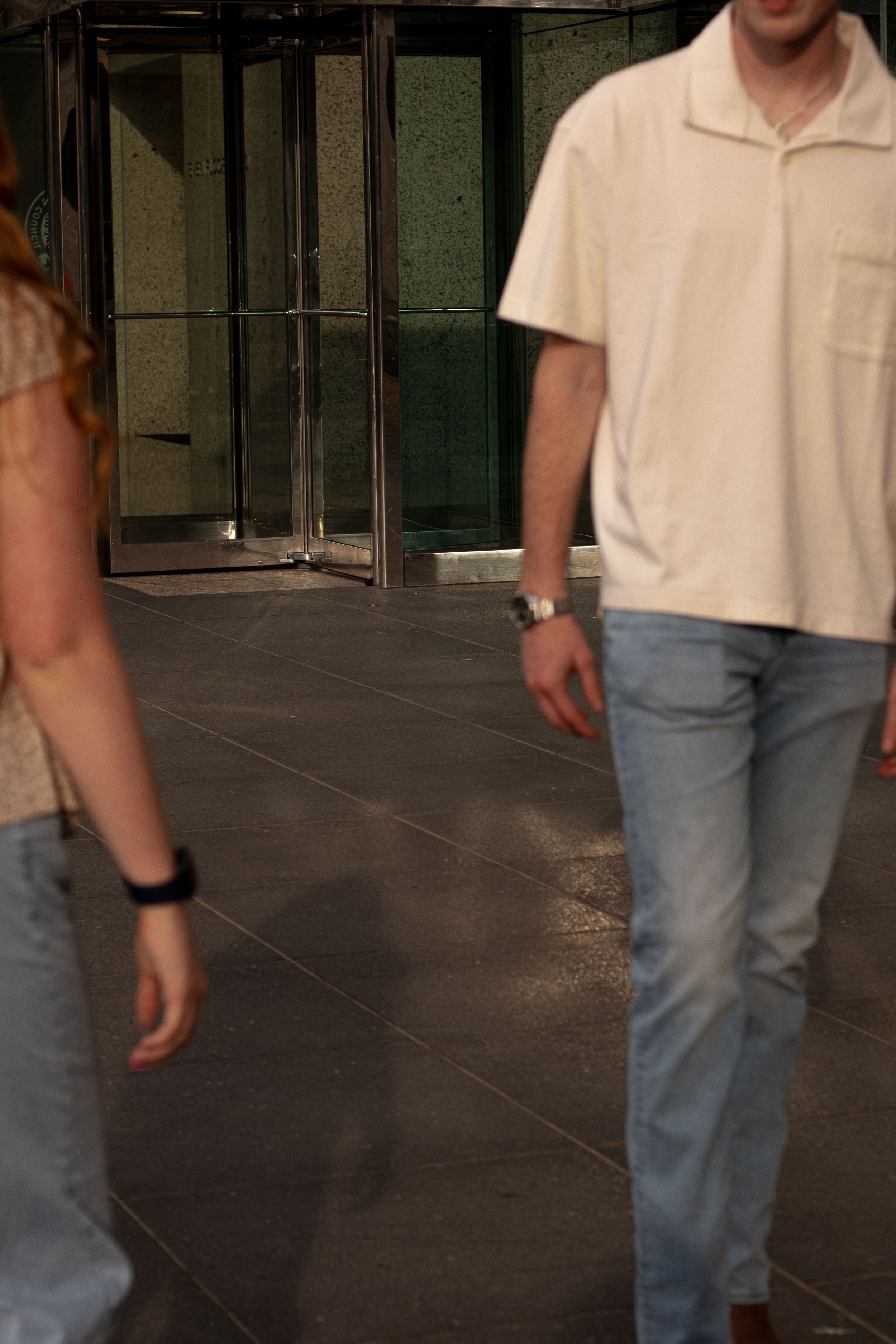 Person walking on dark reflective floor wearing light colored polo shirt and jeans.