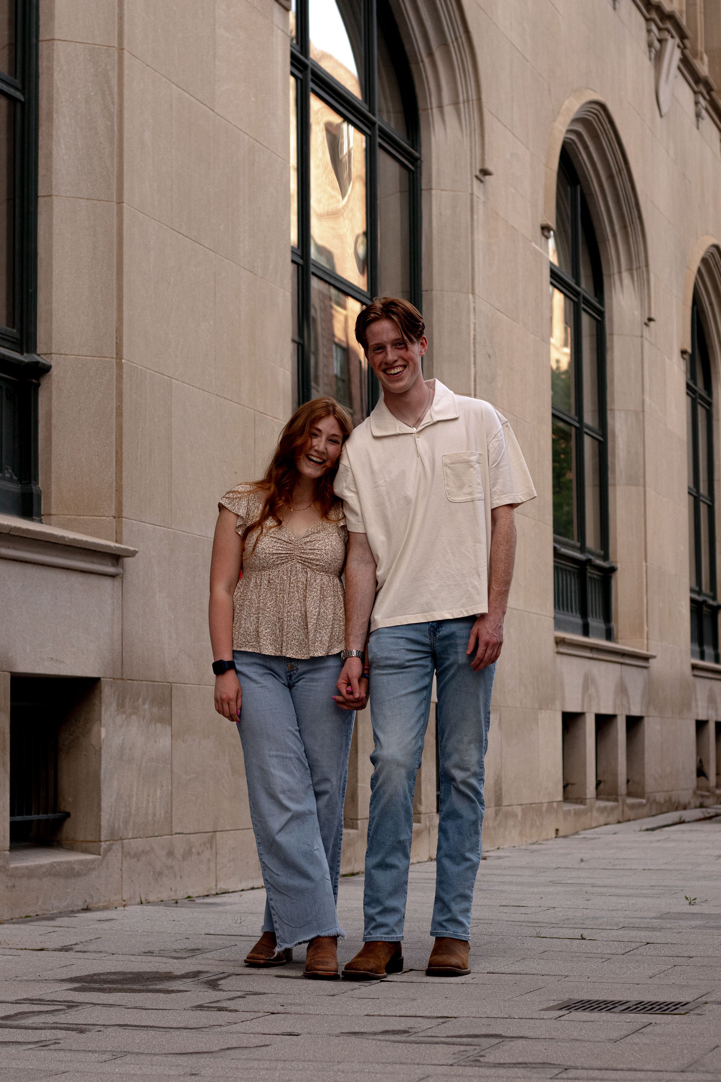 Couple walking together along a stone building exterior with arched windows.