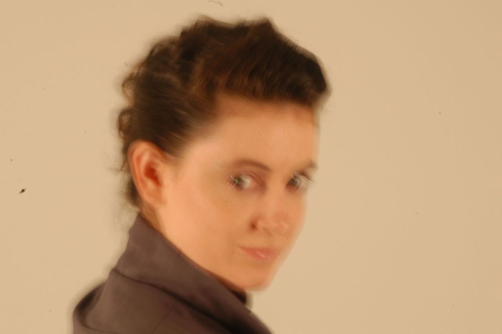 Woman with dark upswept hair in gray turtleneck gazing sideways against light background.