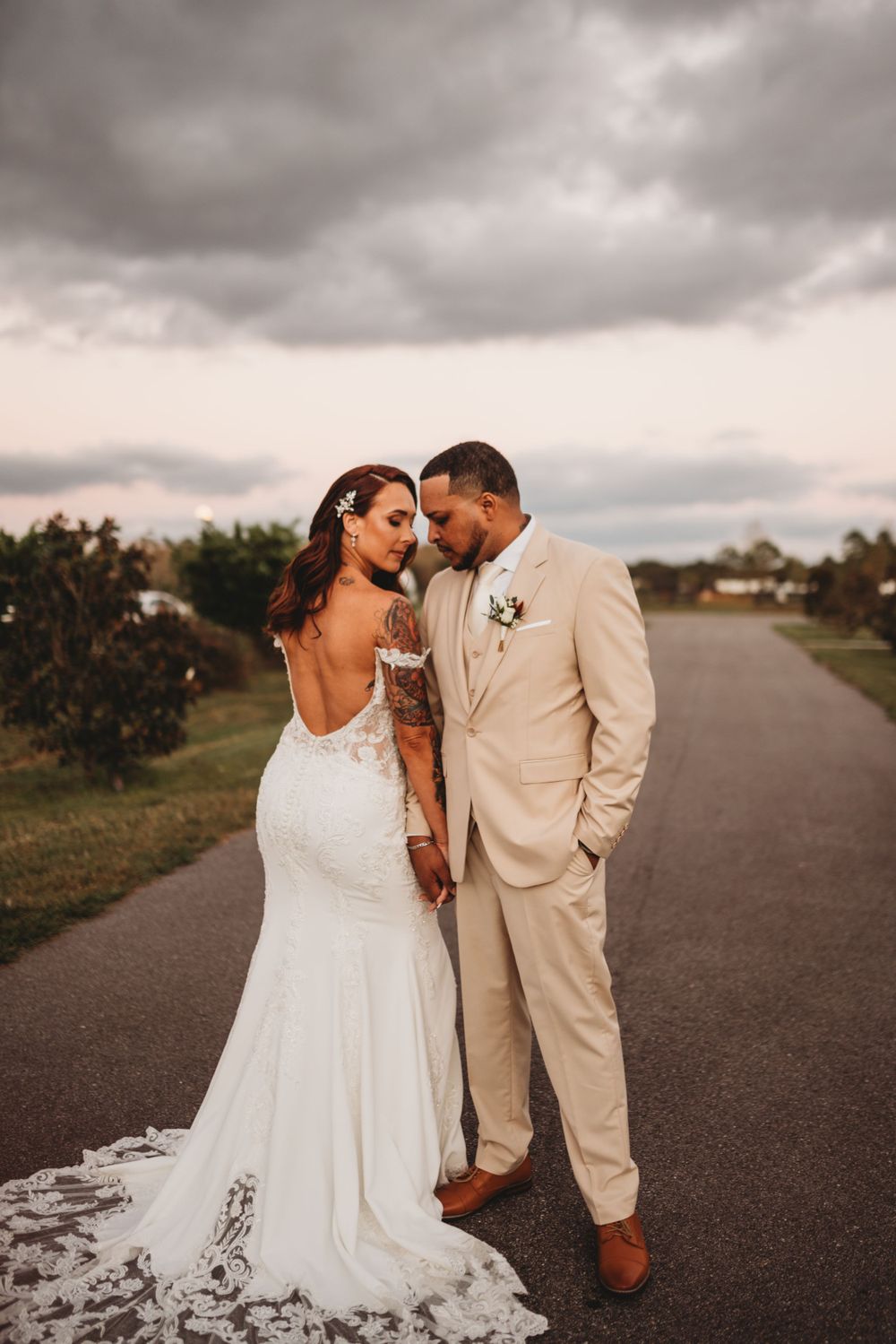 A romantic wedding portrait of a couple in a dreamy outdoor setting with dramatic cloudy skies.