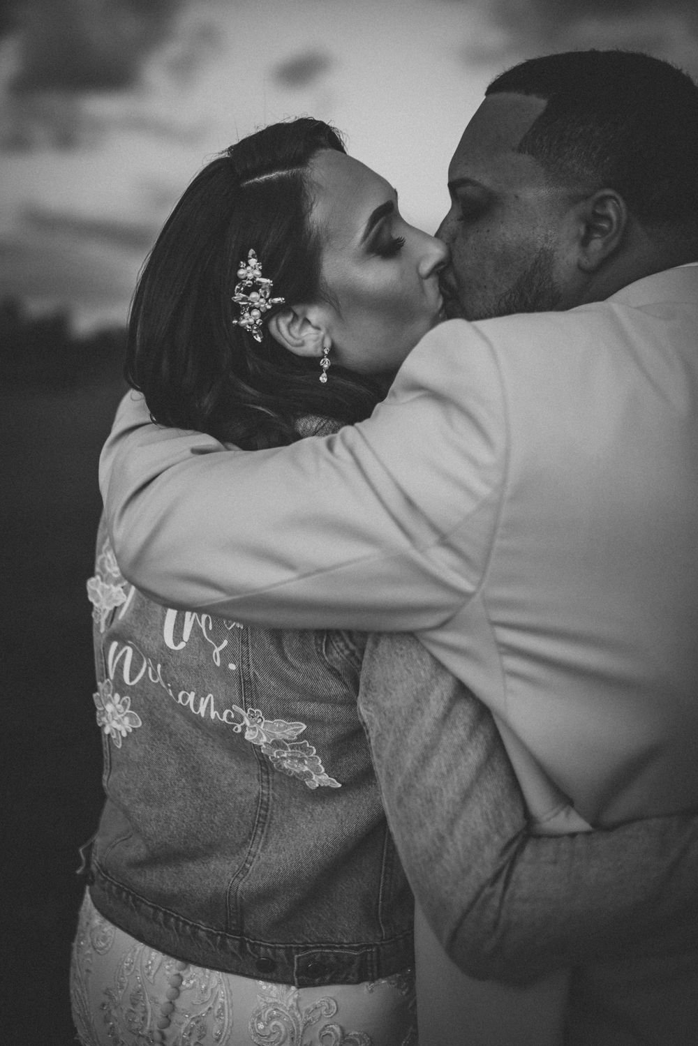 Newlyweds share a tender kiss while the bride wears a personalized denim jacket over her gown.