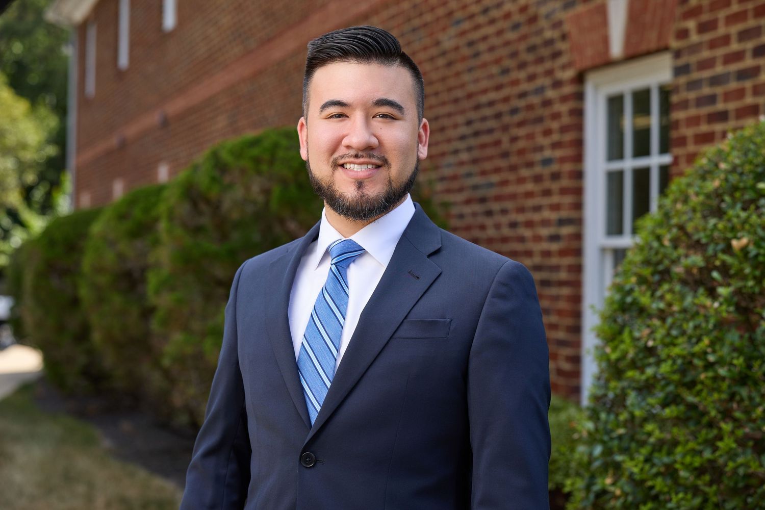 Professional outdoor portrait of someone in navy suit and blue tie against brick building.