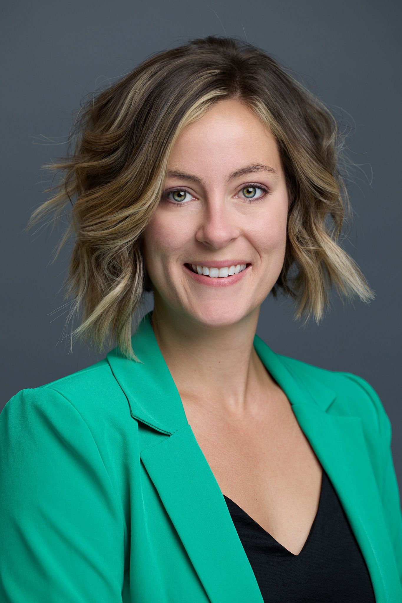 Professional headshot of someone in bright green blazer with wavy blonde hair.