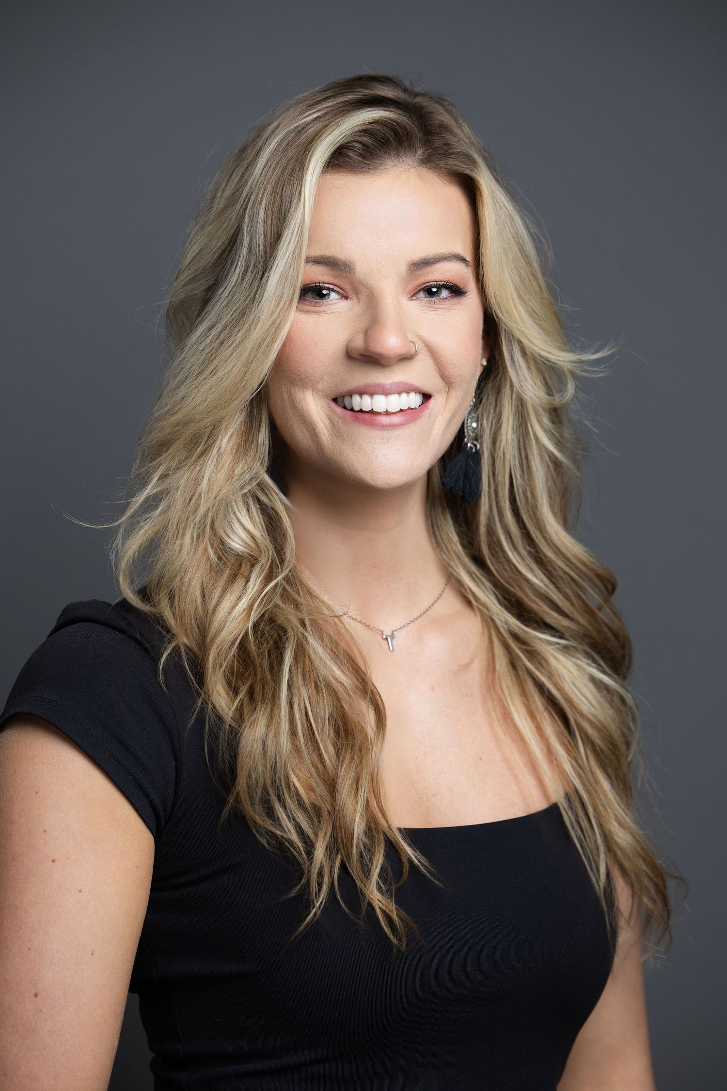 Professional portrait of person in black top with blonde hair against dark background.