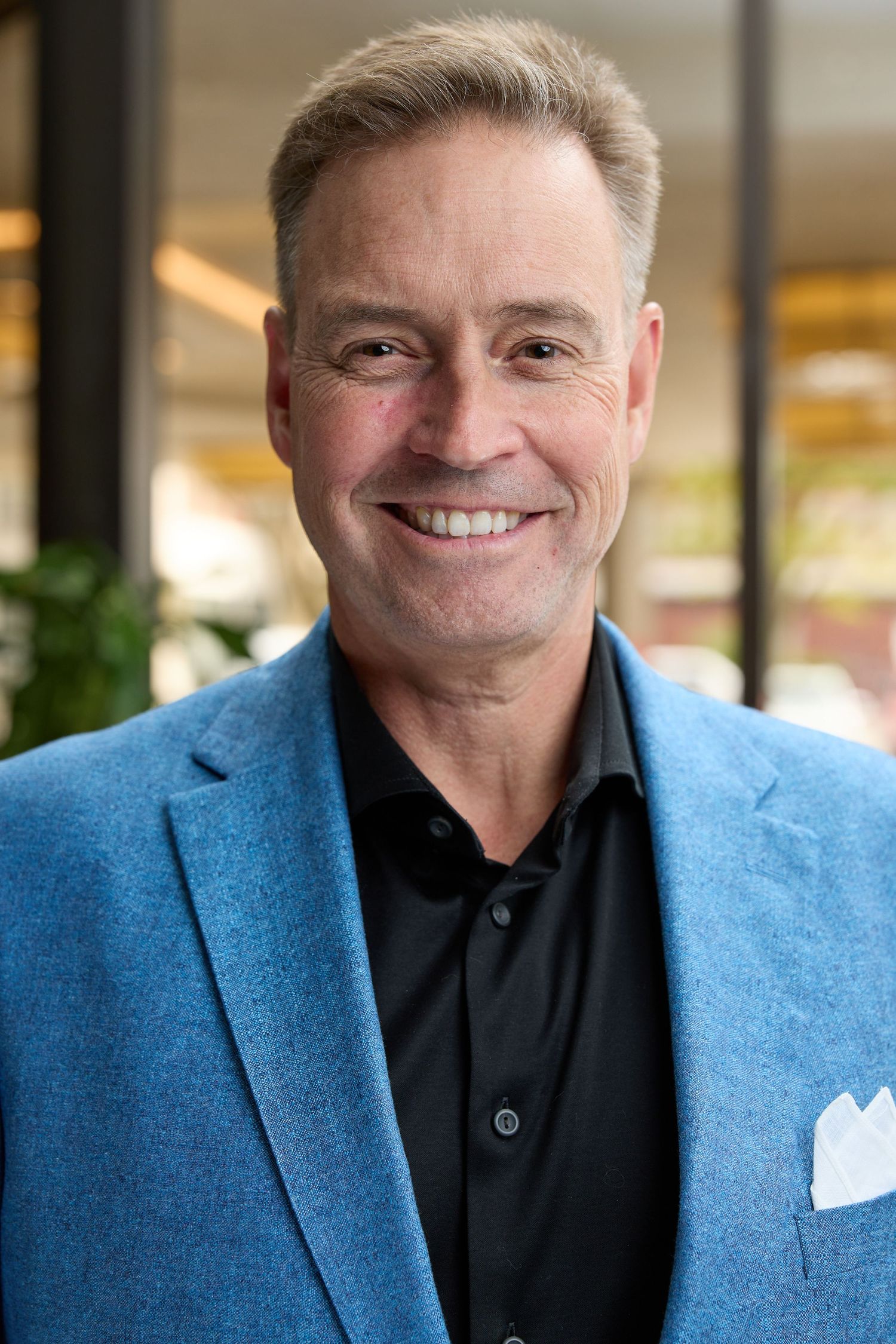 Professional headshot of person in light blue blazer and black shirt.