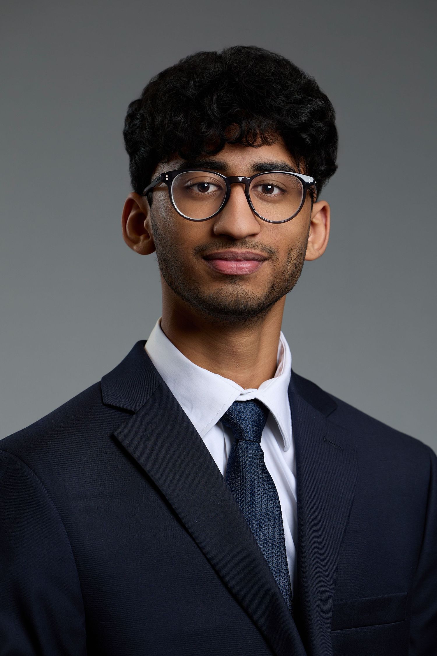 Professional headshot of someone wearing glasses and navy suit with tie.