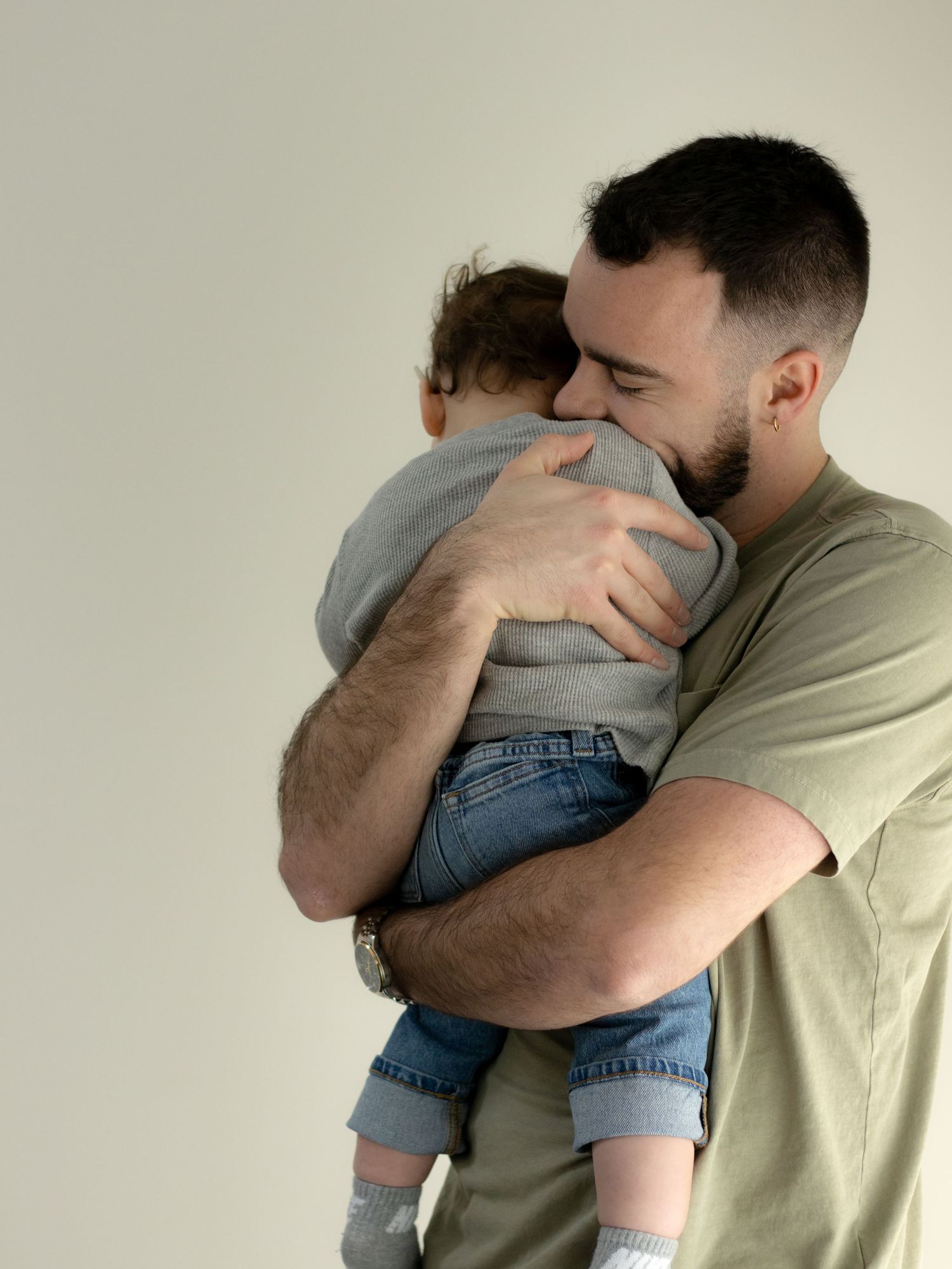 Tender moment between parent and child in casual attire against a neutral background.