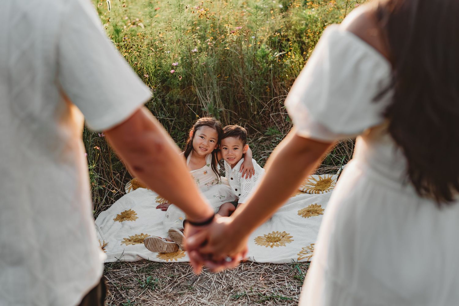 Happy Asian family with laughing baby sits on blanket in golden autumn field.