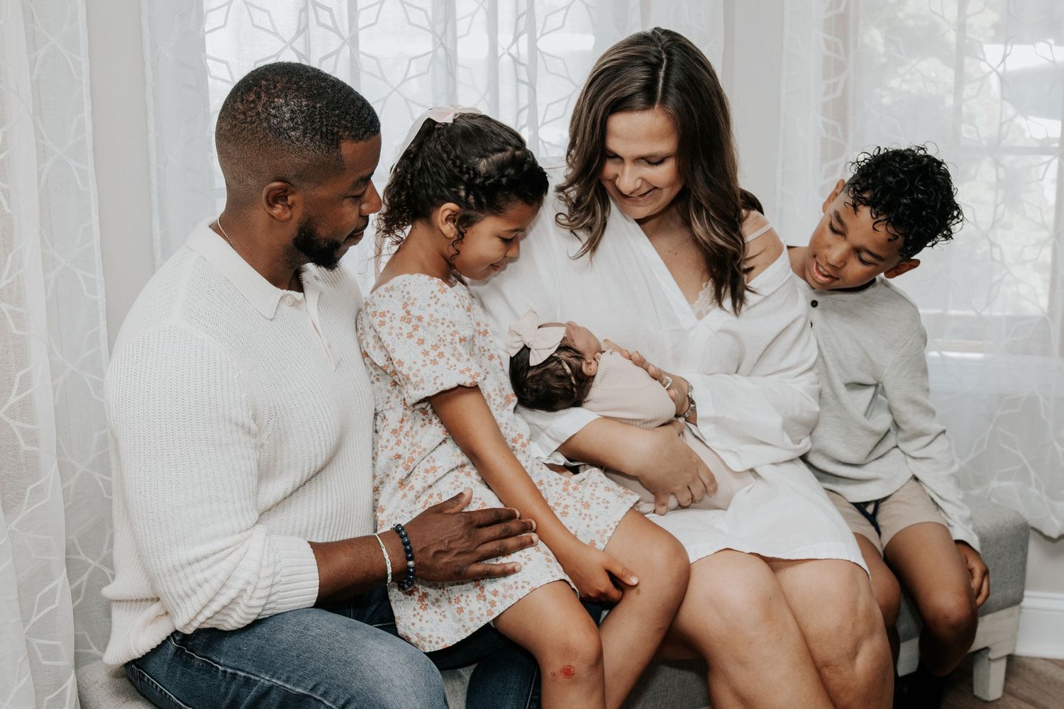 Family wearing white clothes cuddling together on a couch in a bright room.