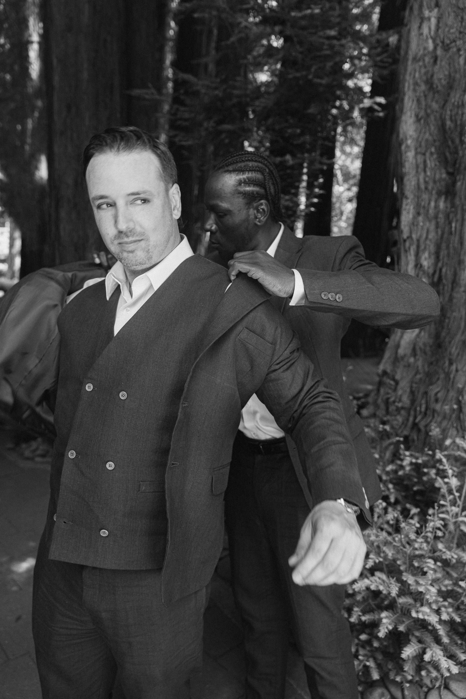 A black and white photo series showing a person in a dark suit posing in a wooded outdoor setting.