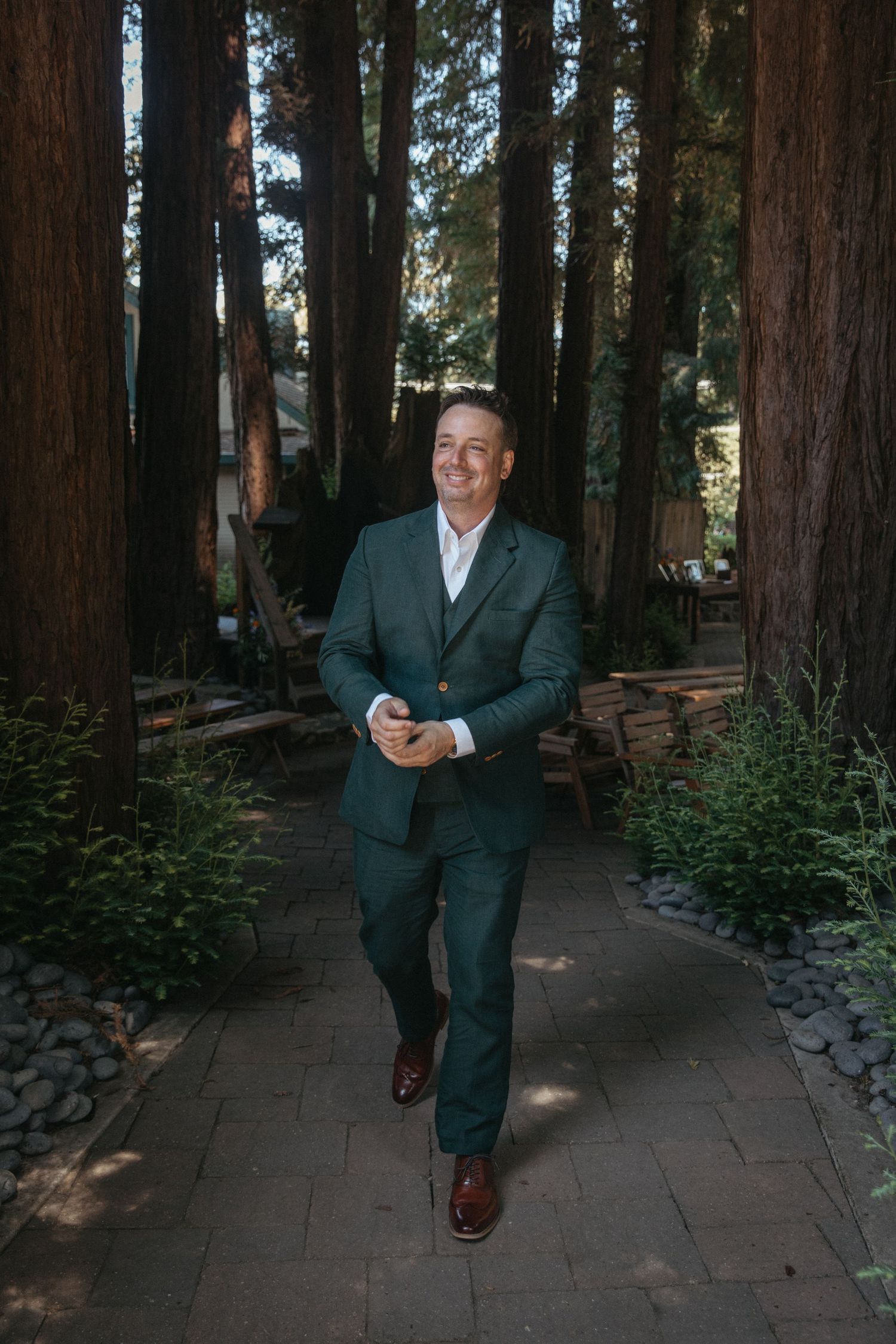 A sequence of photos showing a person in a dark suit walking through a redwood forest setting on a stone path.