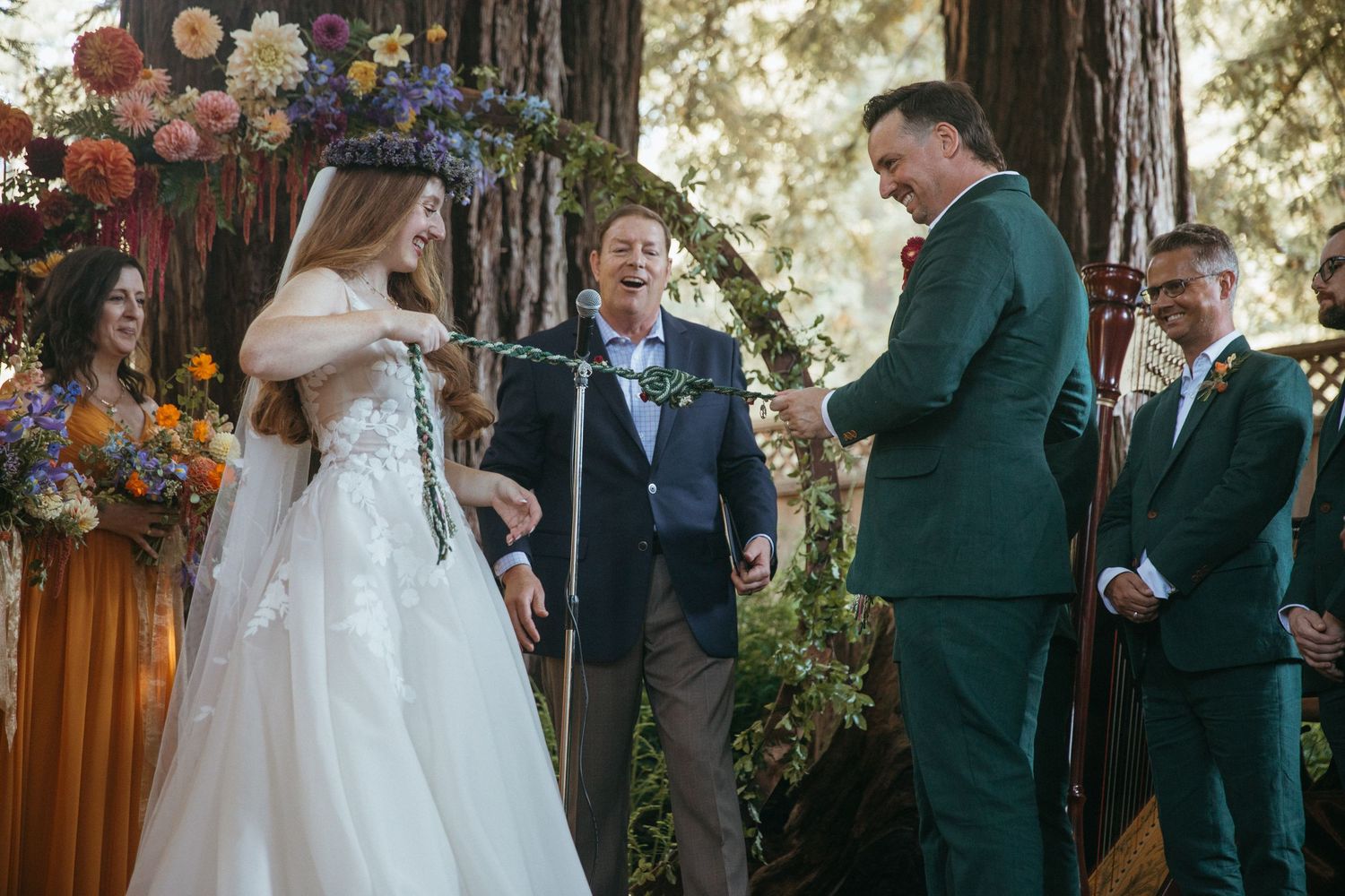 Wedding celebration under tall redwood trees with lantern decorations and guests gathered for an outdoor ceremony.