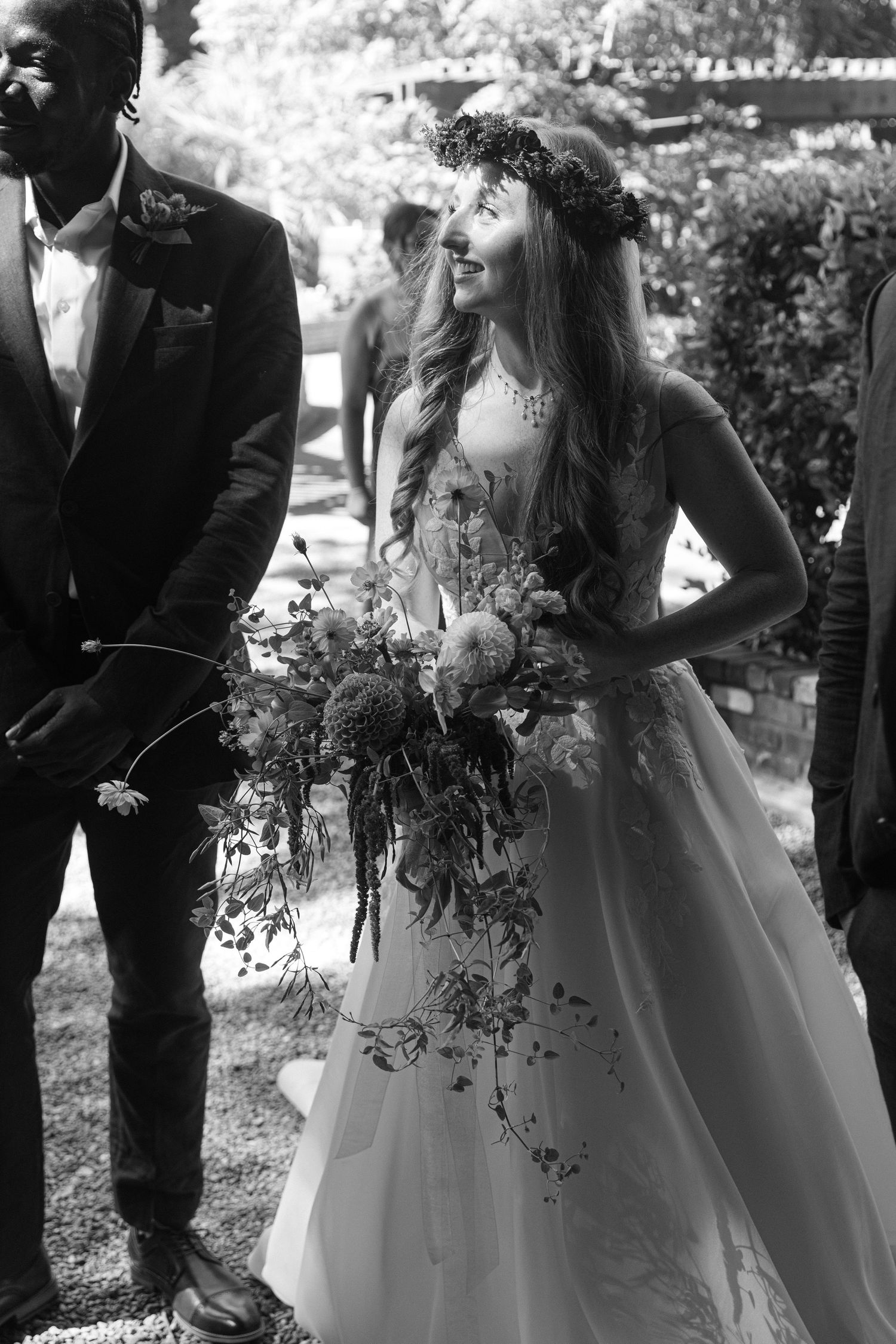 Wedding party poses outdoors with bride in white gown holding cascading floral bouquet.