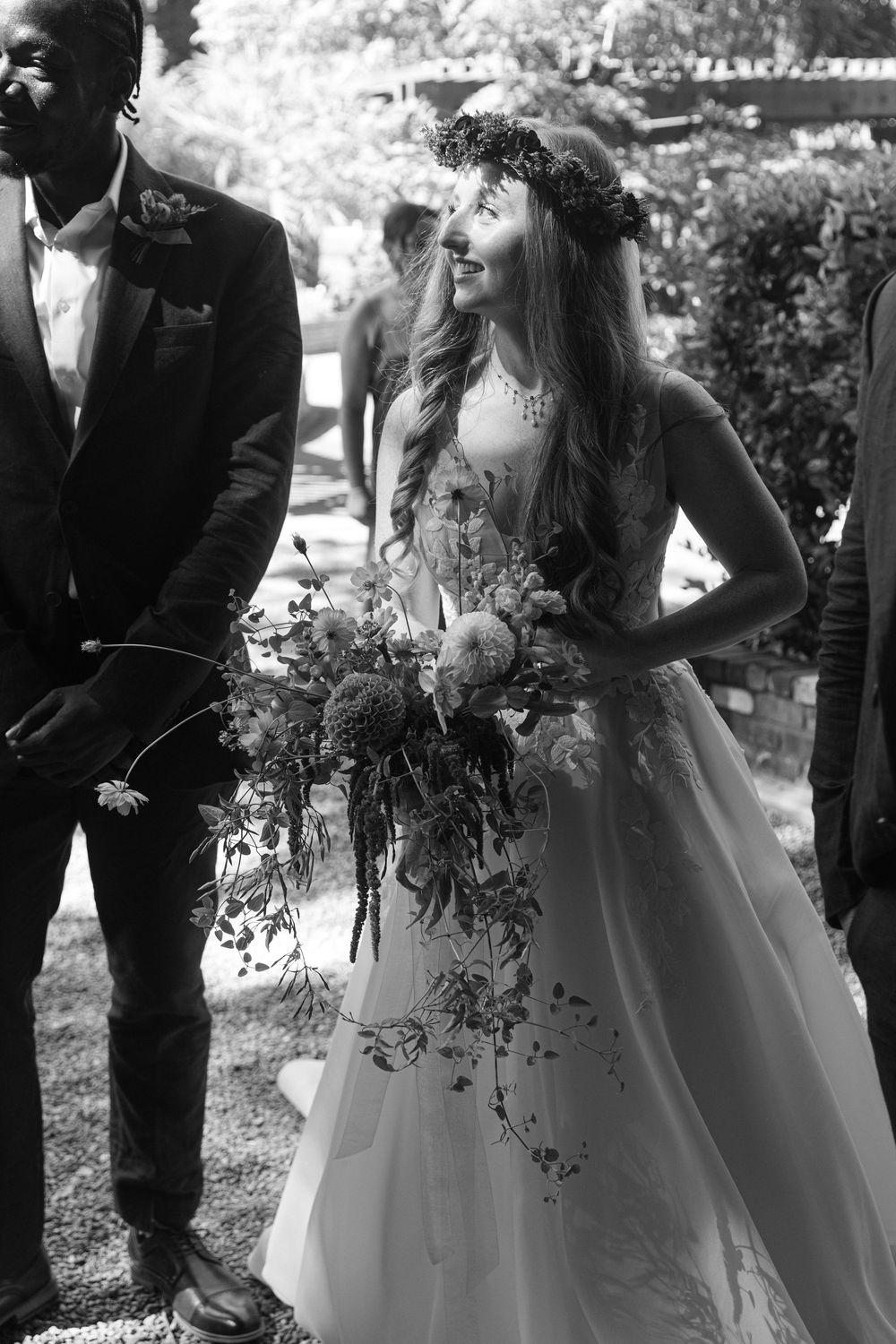 Wedding party poses outdoors with bride in white gown holding cascading floral bouquet.
