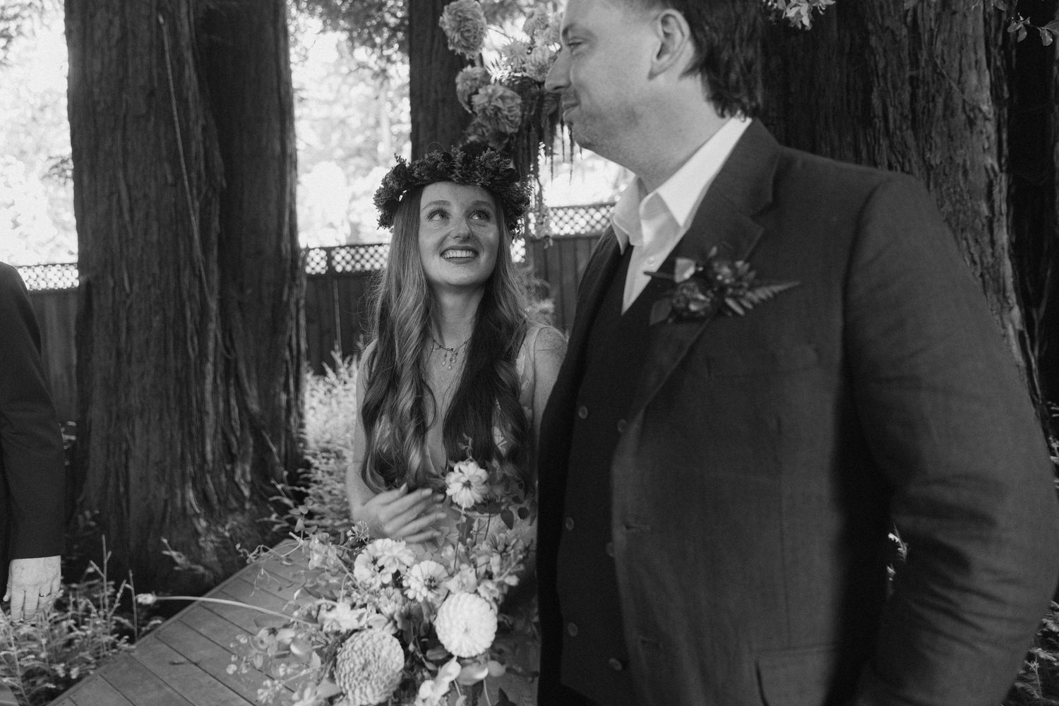 A candid wedding moment captured in black and white against a backdrop of redwood trees.