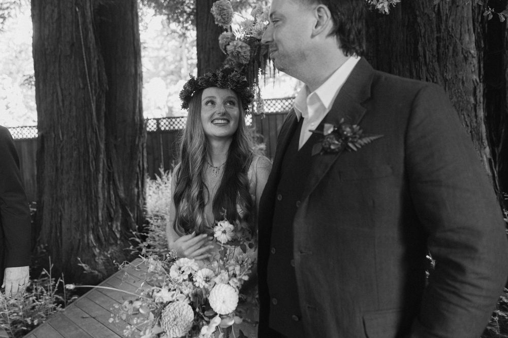 A candid wedding moment captured in black and white against a backdrop of redwood trees.