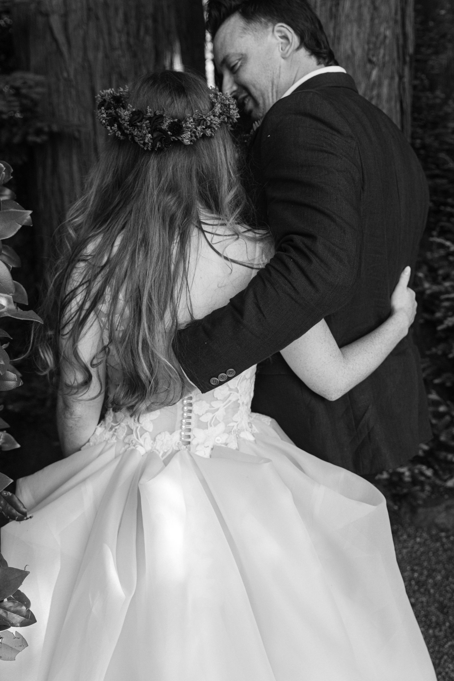 A black and white wedding photo showing a couple embracing, with the bride wearing a floral crown and white dress.