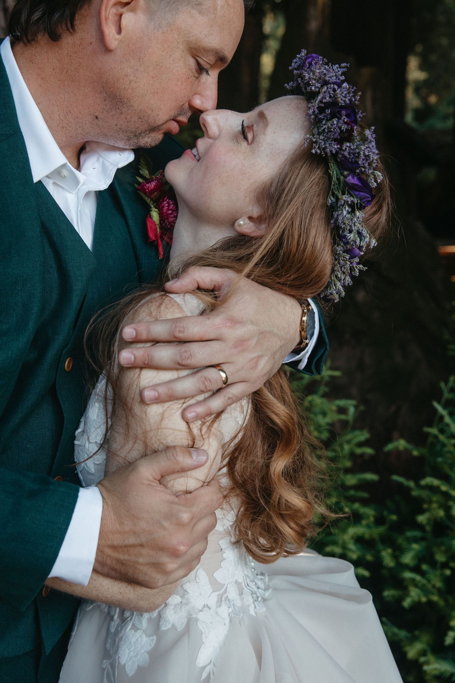 A romantic wedding moment captured in a garden setting with purple floral crown details.