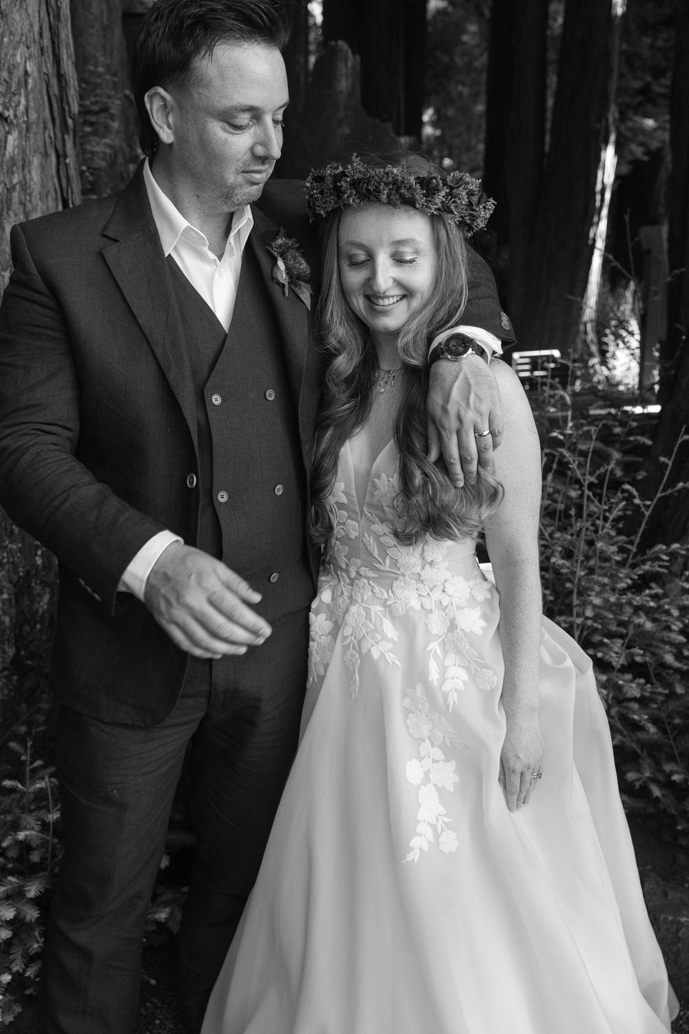 Newlyweds share candid moments in a serene redwood forest setting.