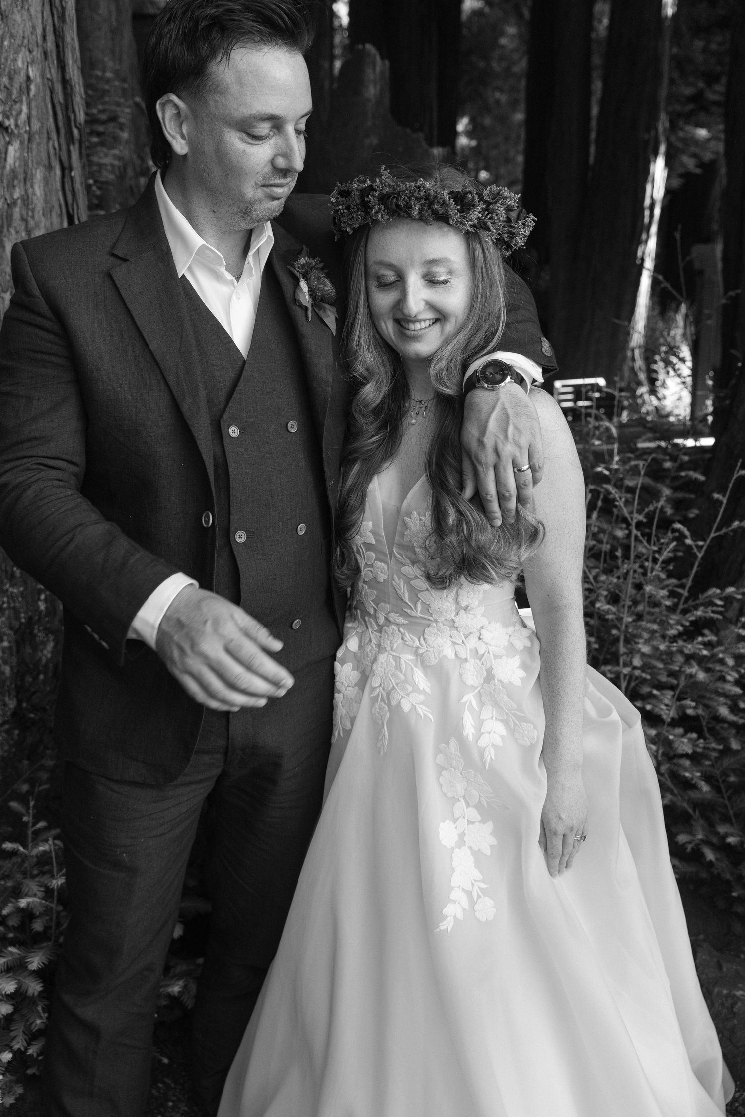 Newlyweds share candid moments in a serene redwood forest setting.