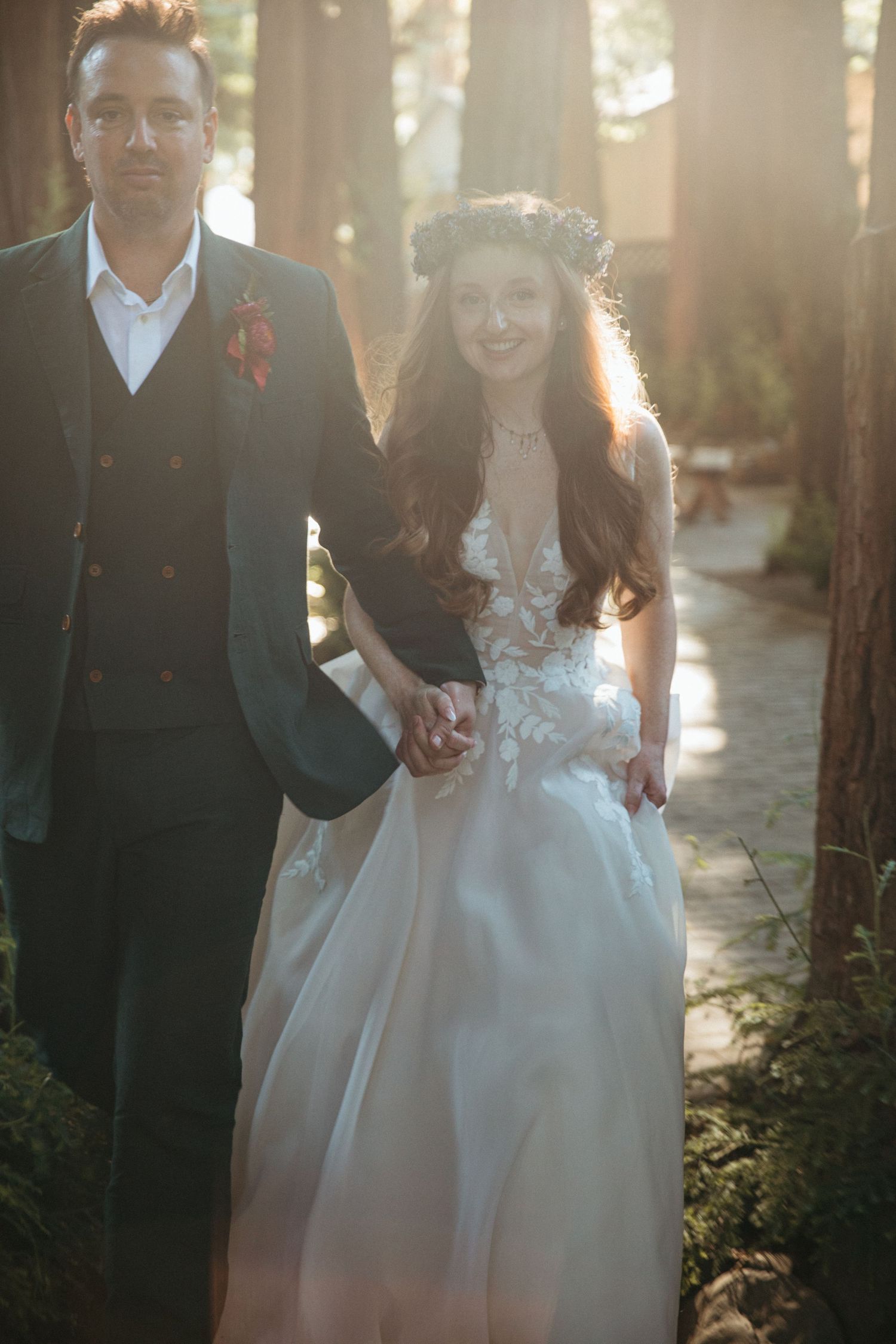 Golden sunlight filters through redwood trees as couple poses for wedding portraits.