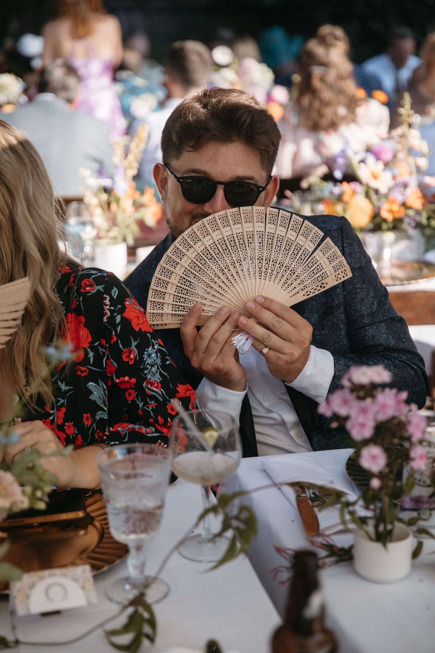 Wedding guests holding decorative hand fans while seated at an elegantly decorated reception table.