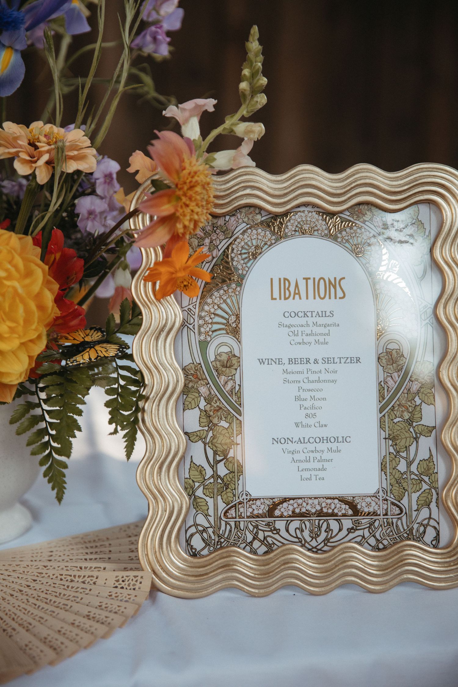 Elegant wedding drink menu signs with wavy frames and floral decorations displayed at a reception.
